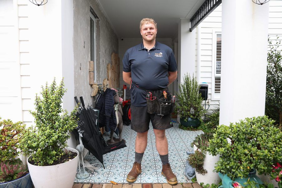 Smiling Curran technician with tool belt at a customer's front door